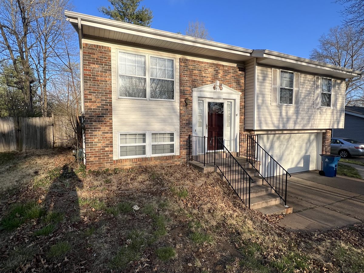 Brick and siding split-level in Ballwin, MO, when Swift Home Buys bought it, with a leaf-covered, overgrown front yard