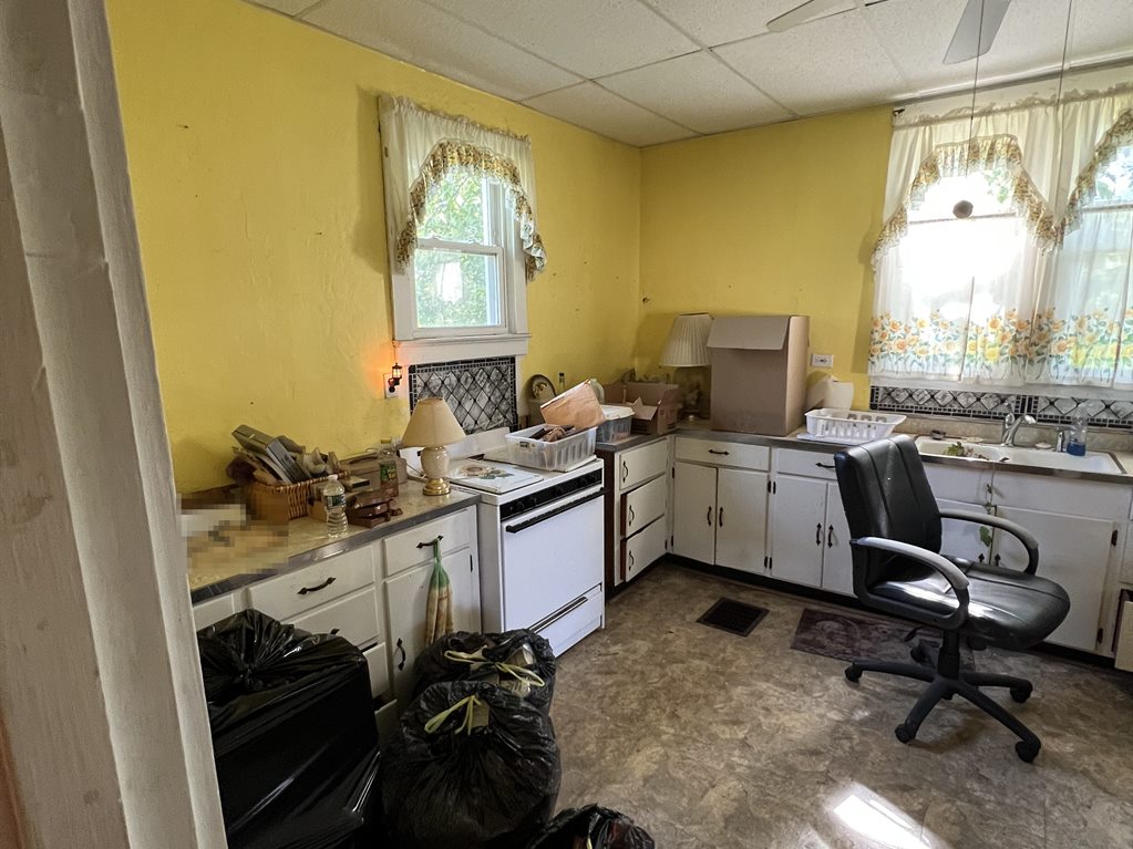Lemay kitchen before: yellow walls, a drop ceiling, old white cabinets and belongings piled on the counters and floor