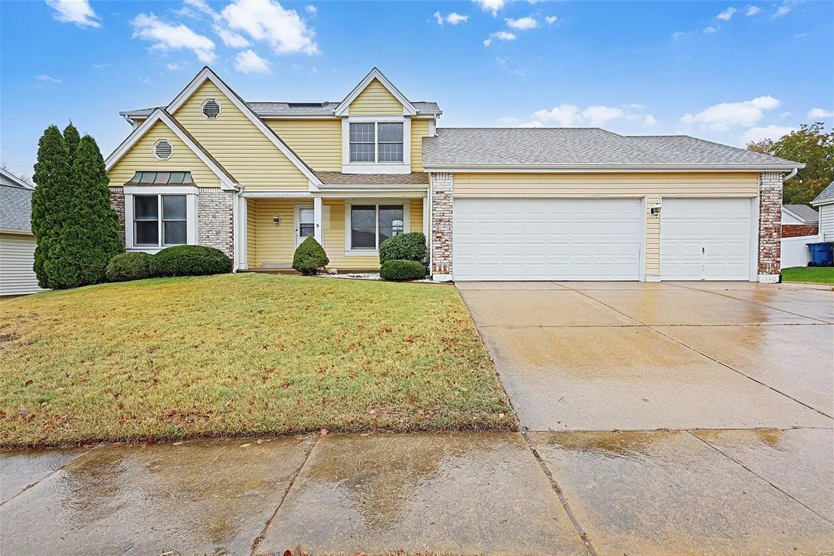 Yellow two-story house with a three-car garage in Oakville, MO, after Swift Home Buys bought it and cleaned it out