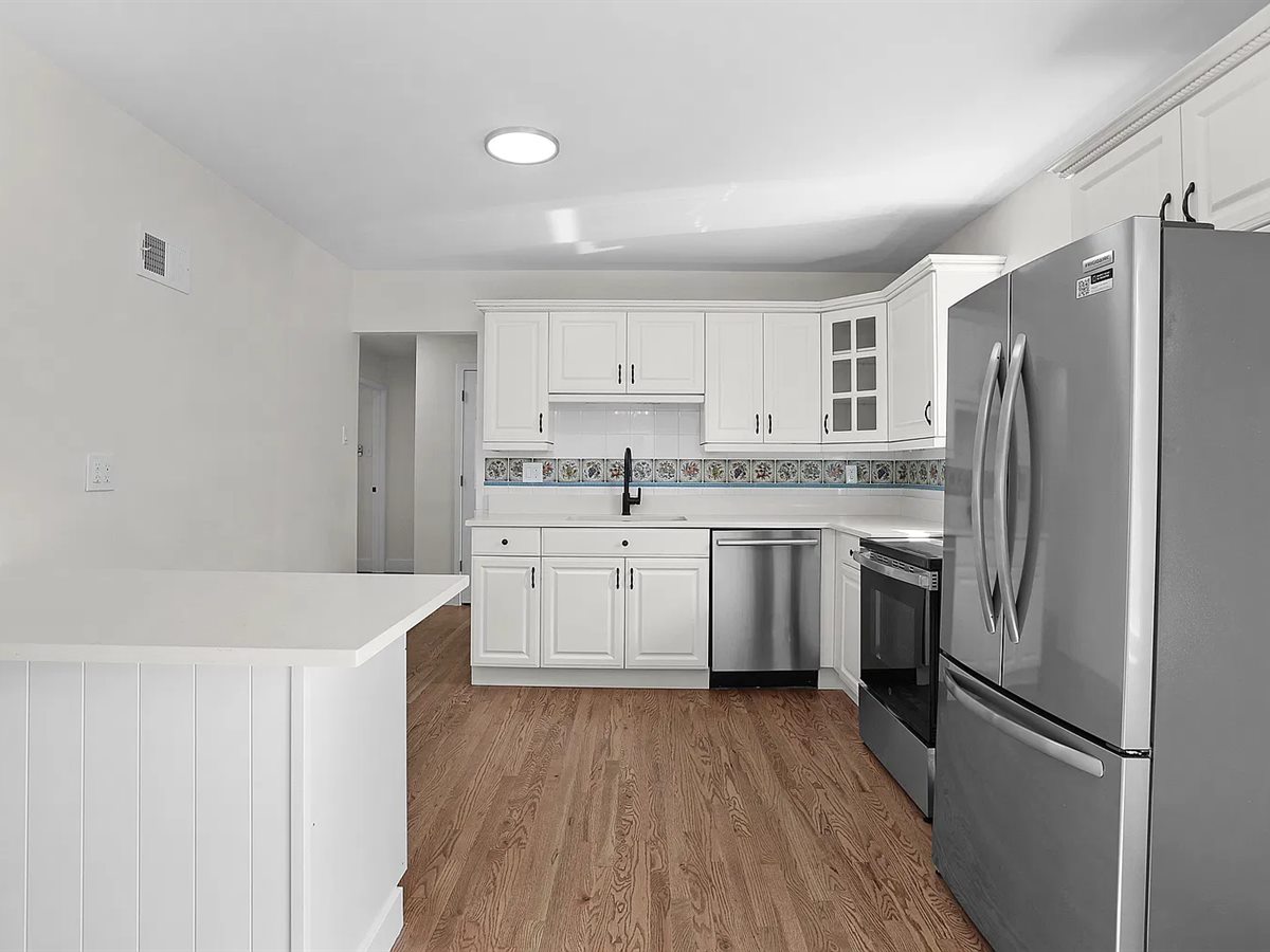 Sunset Hills kitchen after it was opened up: white cabinets, a white peninsula, stainless appliances and refinished hardwood