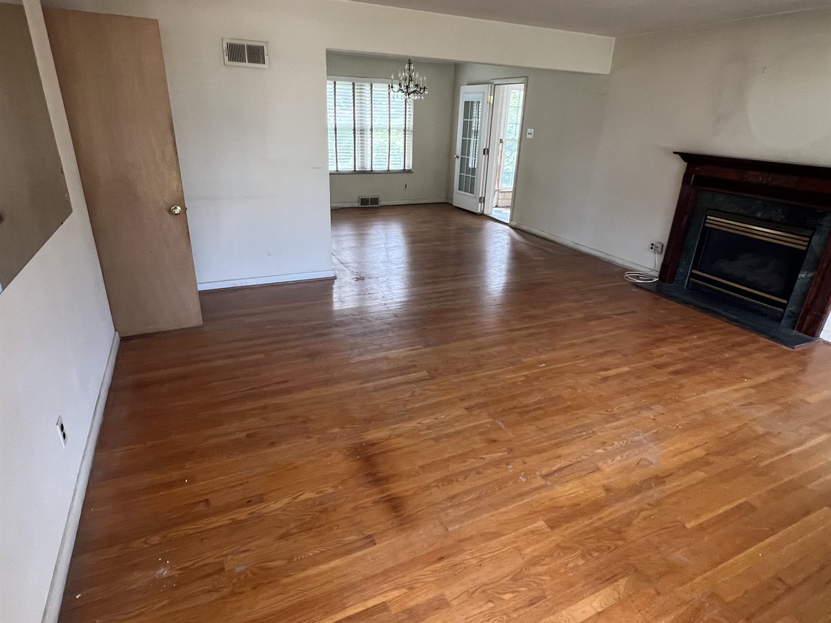 Sunset Hills living room before: worn, patched hardwood floor and dingy walls around the fireplace