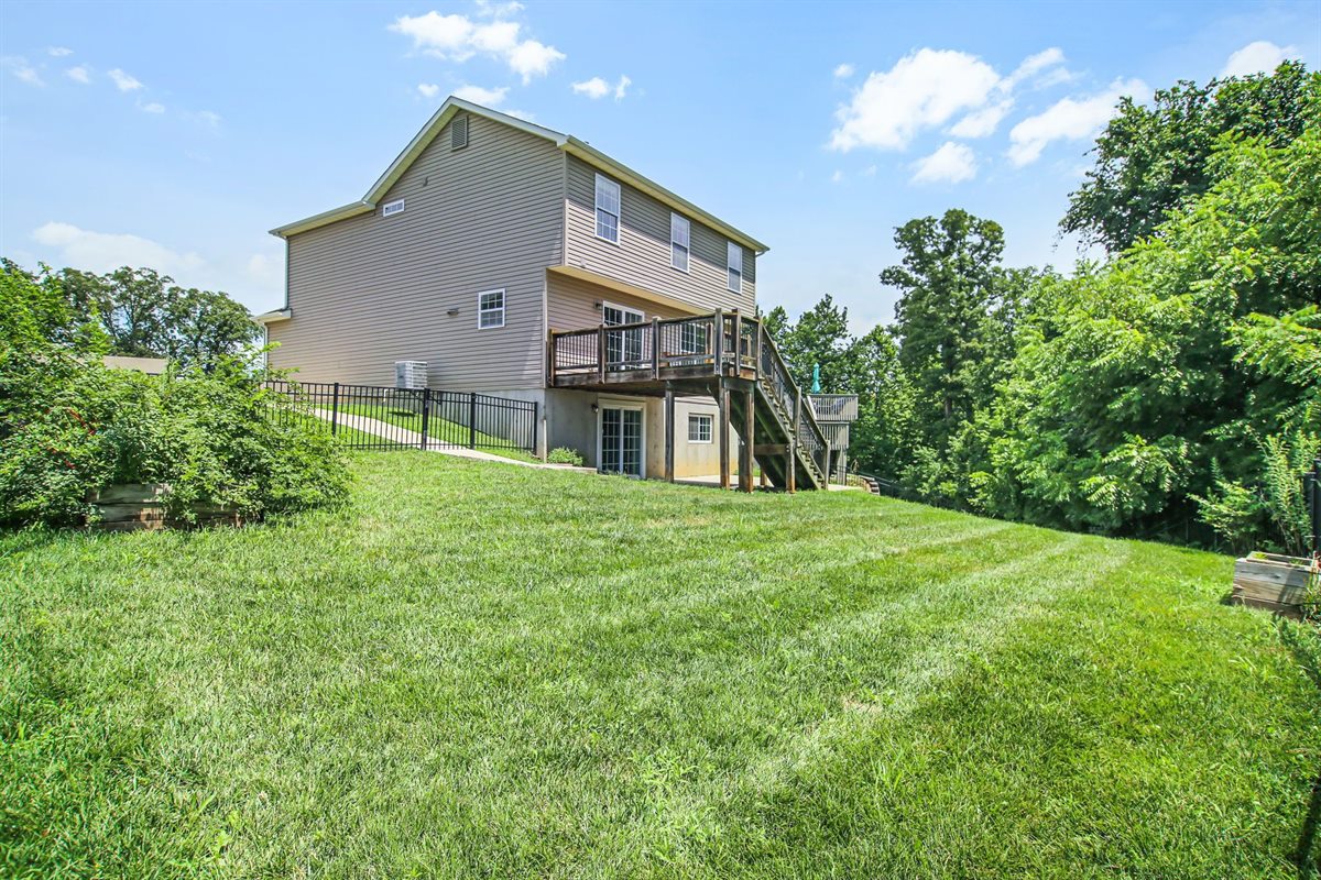 Back of the Wentzville house with a deck, walkout basement and a large green yard backing to trees